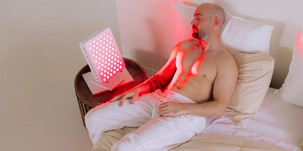 Persoon op bed naast een Liroma Compact roodlichtlamp op het nachtkastje